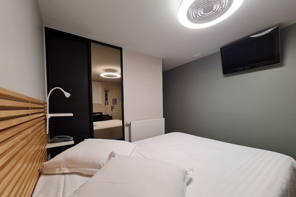 A hotel room with a bed, a mirror, a TV, and a radiator.