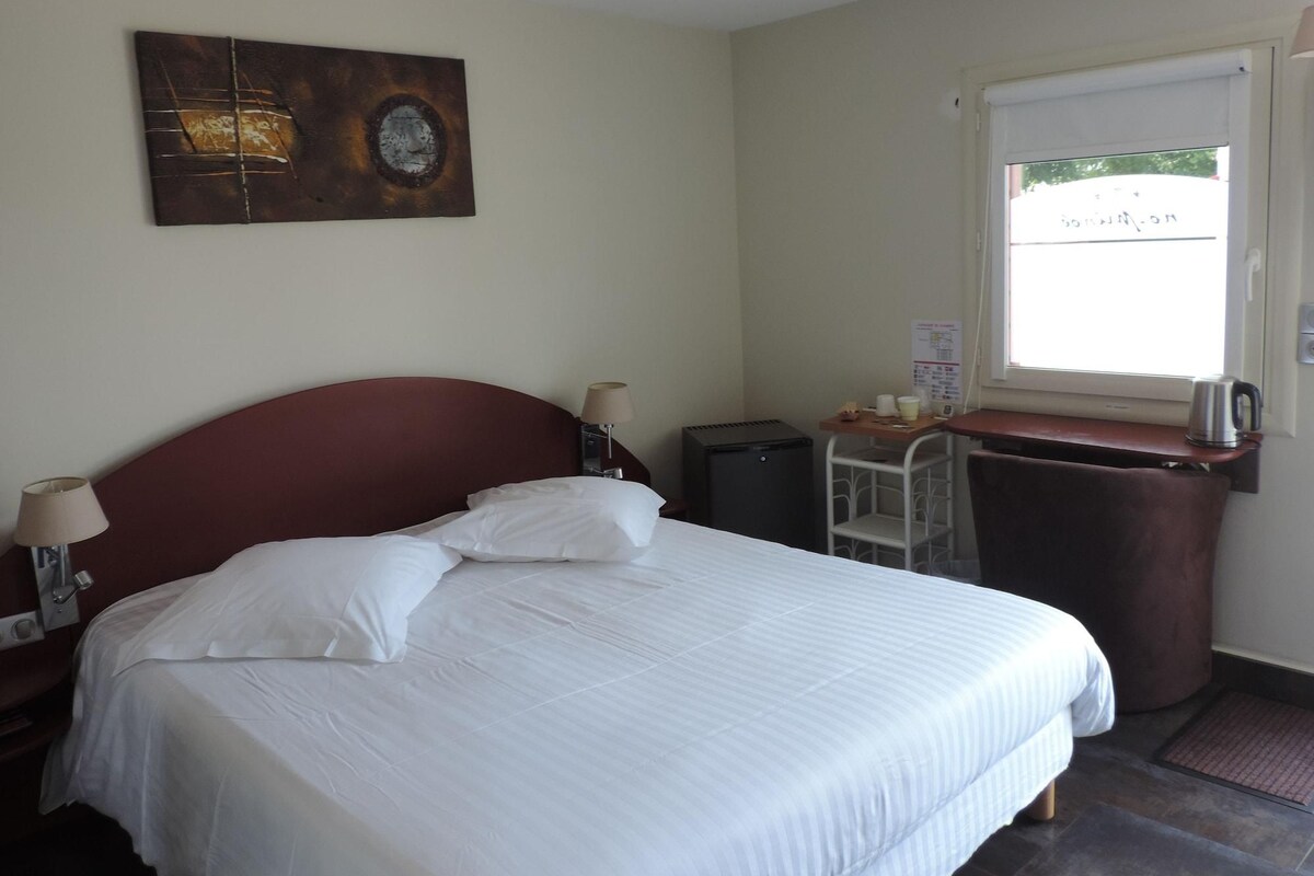 Ein Hotelzimmer mit einem Bett, einem Schreibtisch mit Wasserkocher, einem kleinen Schrank und einem Fenster.