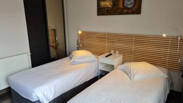 Une chambre d’hôtel avec deux lits simples, une tête de lit en bois, une table de chevet avec une lampe et une œuvre d’art accrochée au mur.