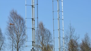 Dos estructuras cilíndricas altas con bandas horizontales, sobre un cielo azul despejado y rodeadas de árboles sin hojas.