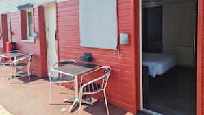 Un edificio rojo con una cama, una mesa y una silla afuera.
