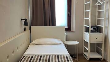 Un dormitorio con cama, mesita de noche, armario y ventana con cortinas.