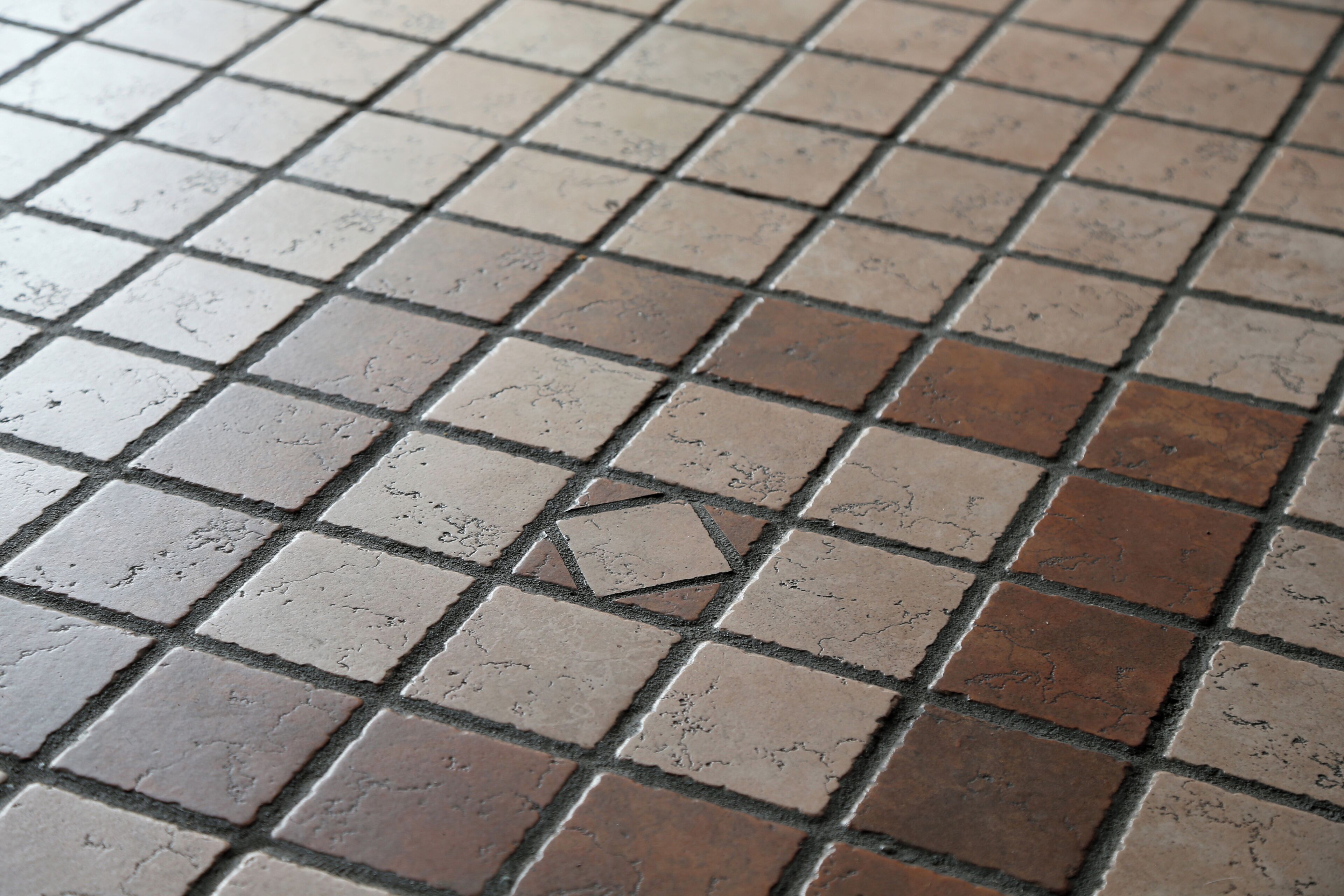 A close-up of a tiled floor with a pattern of square tiles in varying shades of brown and beige.