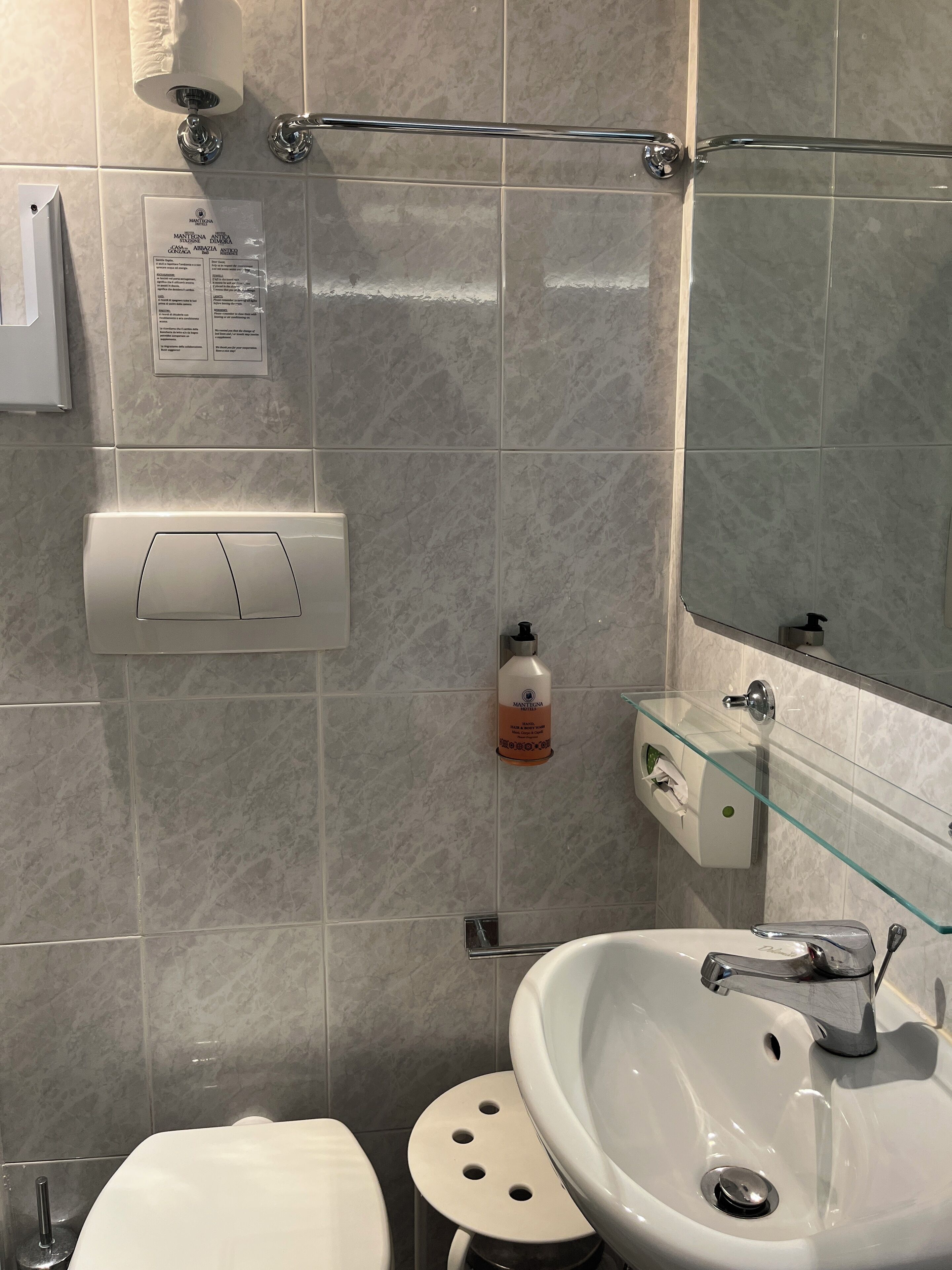 Un baño con un lavabo blanco, un dispensador de jabón de vidrio, un inodoro y un secador de manos.