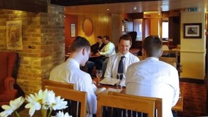 Een restaurant met bakstenen muren, houten balken en gasten aan tafels.