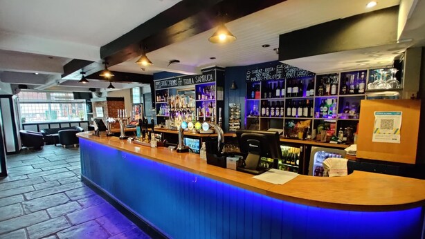 Een bar met een toonbank, barstoelen en diverse flessen en glazen.