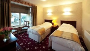Een hotelkamer met twee eenpersoonsbedden, een bureau met stoel, een raam met gordijnen en een lampje op het nachtkastje.
