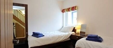 Un dormitorio pequeño y bien iluminado con dos camas individuales, un aparador de madera, un espejo y una ventana con cortinas.