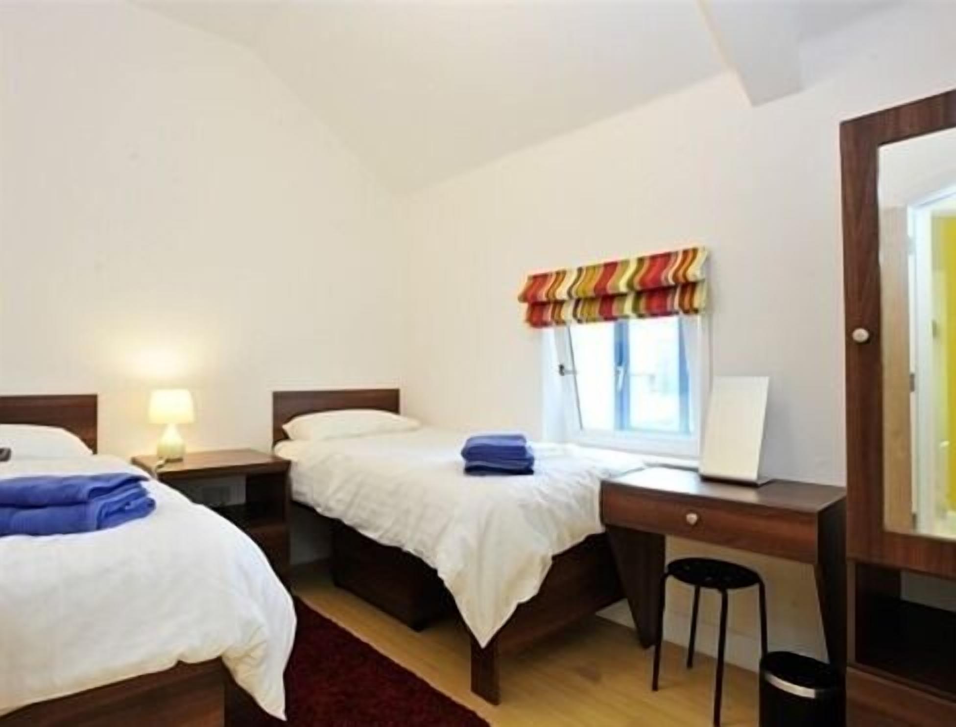 A hotel room with two beds, a desk, a chair, a lamp, and a window with a striped valance.