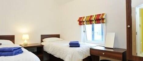 A hotel room with two beds, a desk, a chair, a lamp, and a window with a striped valance.