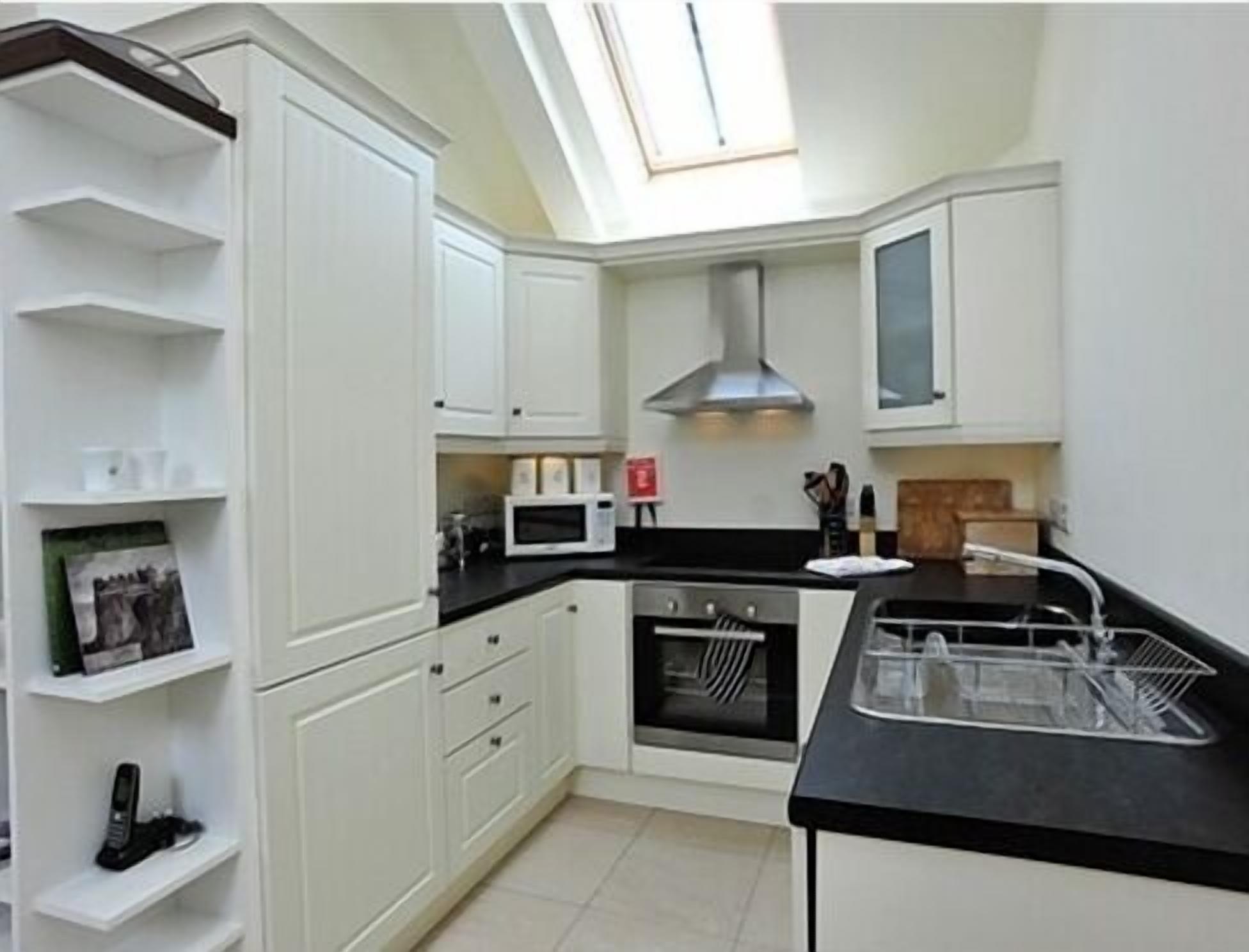 A compact kitchen with white cabinets, a microwave, oven, and a black countertop.