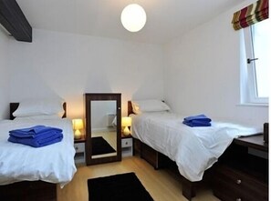 A small, clean room with two single beds, a mirror, bedside lamps, and a window with curtains.