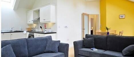 A modern apartment with two grey sofas, a kitchen with white cabinets, and a yellow accent wall.
