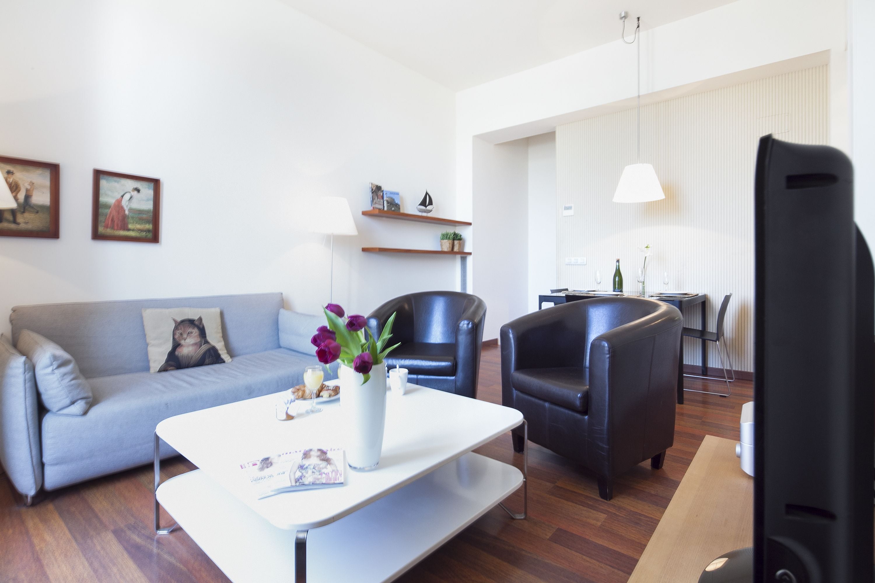 A modern living room with a grey sofa, a white coffee table, and two black armchairs. There is a small table with a lamp and a few decorative items.