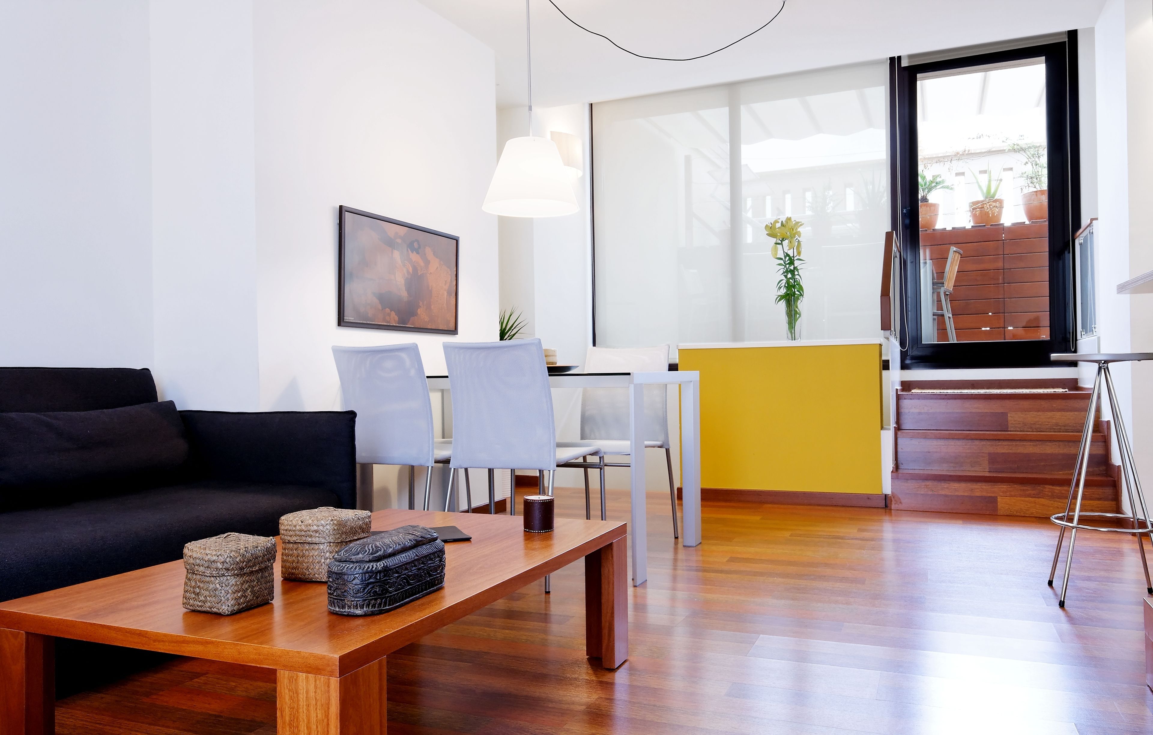 A modern living room with a black sofa, wooden coffee table, and a dining area with a yellow accent wall.