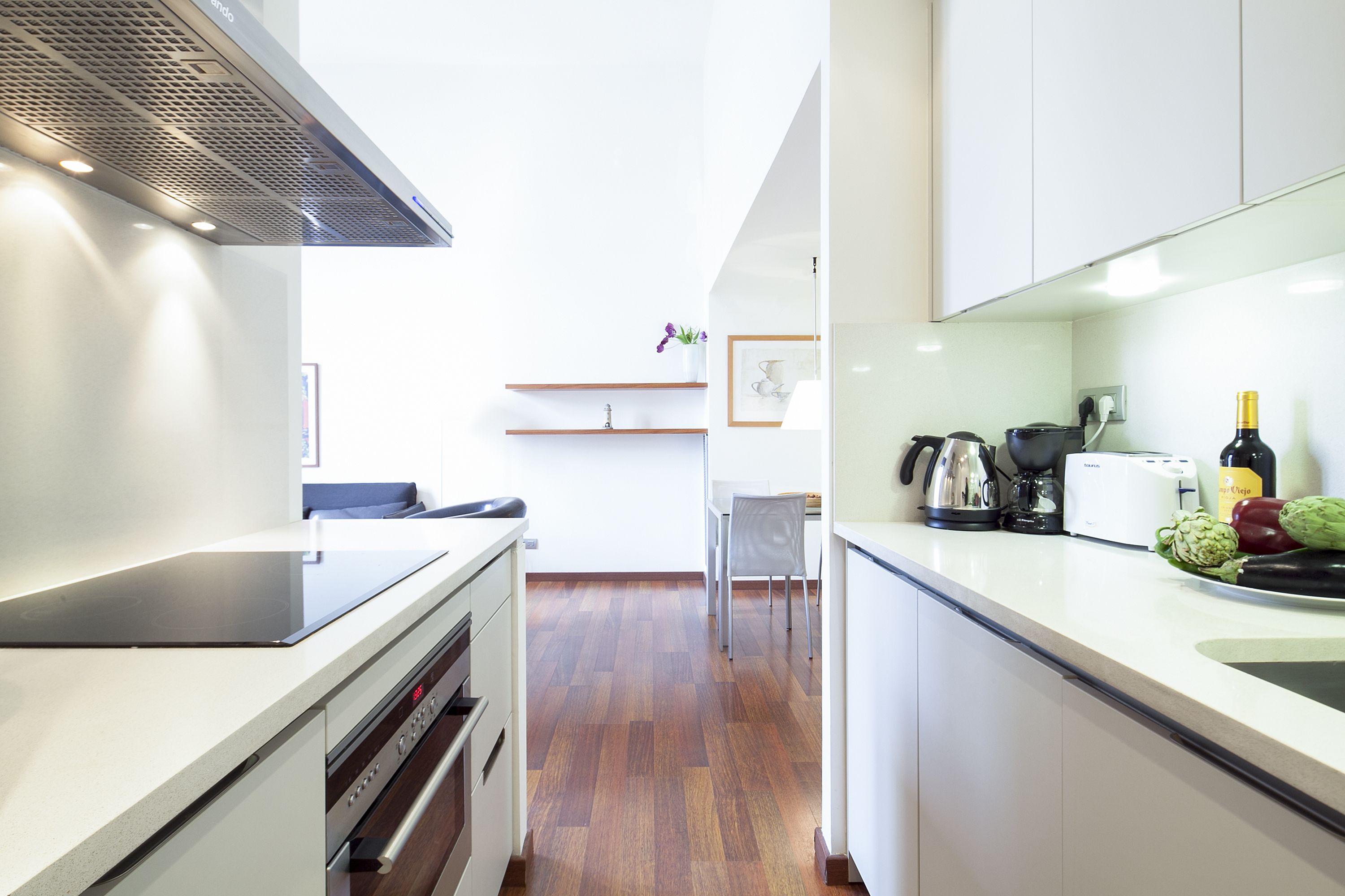 A modern kitchen with white cabinets, a stainless steel range hood, and a wooden floor.