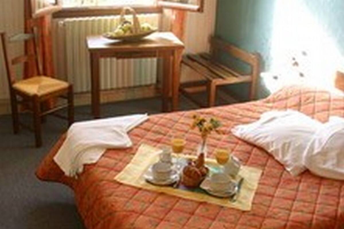 A hotel room with a bed, a dining table with chairs, a window with curtains, and a wall-mounted light fixture.