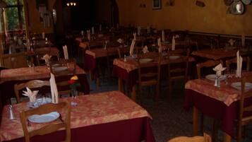 A restaurant with multiple tables set for dining, featuring wooden chairs and red tablecloths.