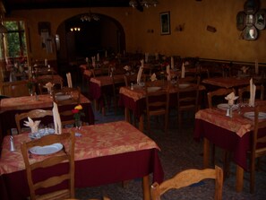 A restaurant with multiple tables set for dining, featuring wooden chairs and red tablecloths. - Au Gai Soleil du Mont Aiguille (Chichilianne)