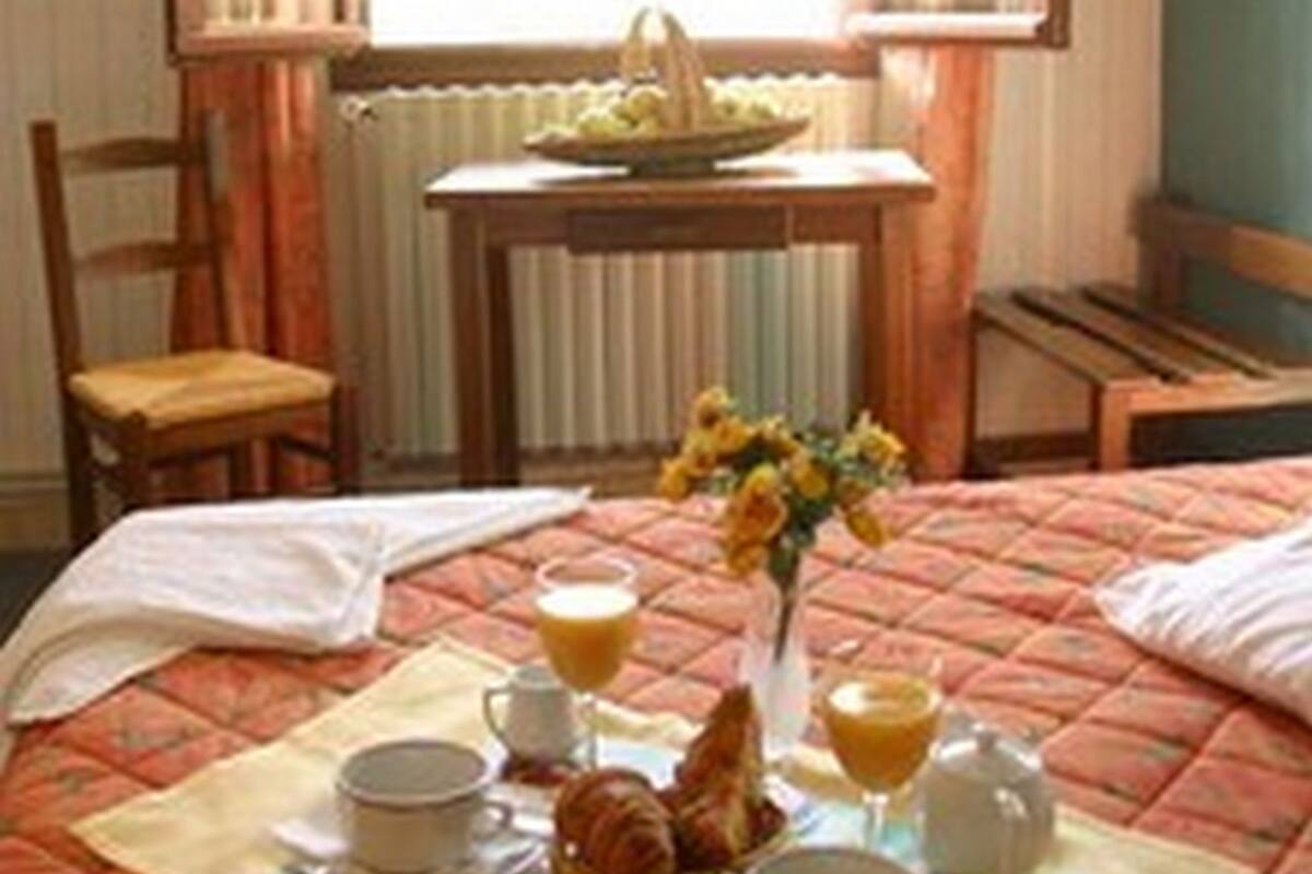 A neatly made bed with a breakfast setup including croissants, orange juice, and a vase of flowers.