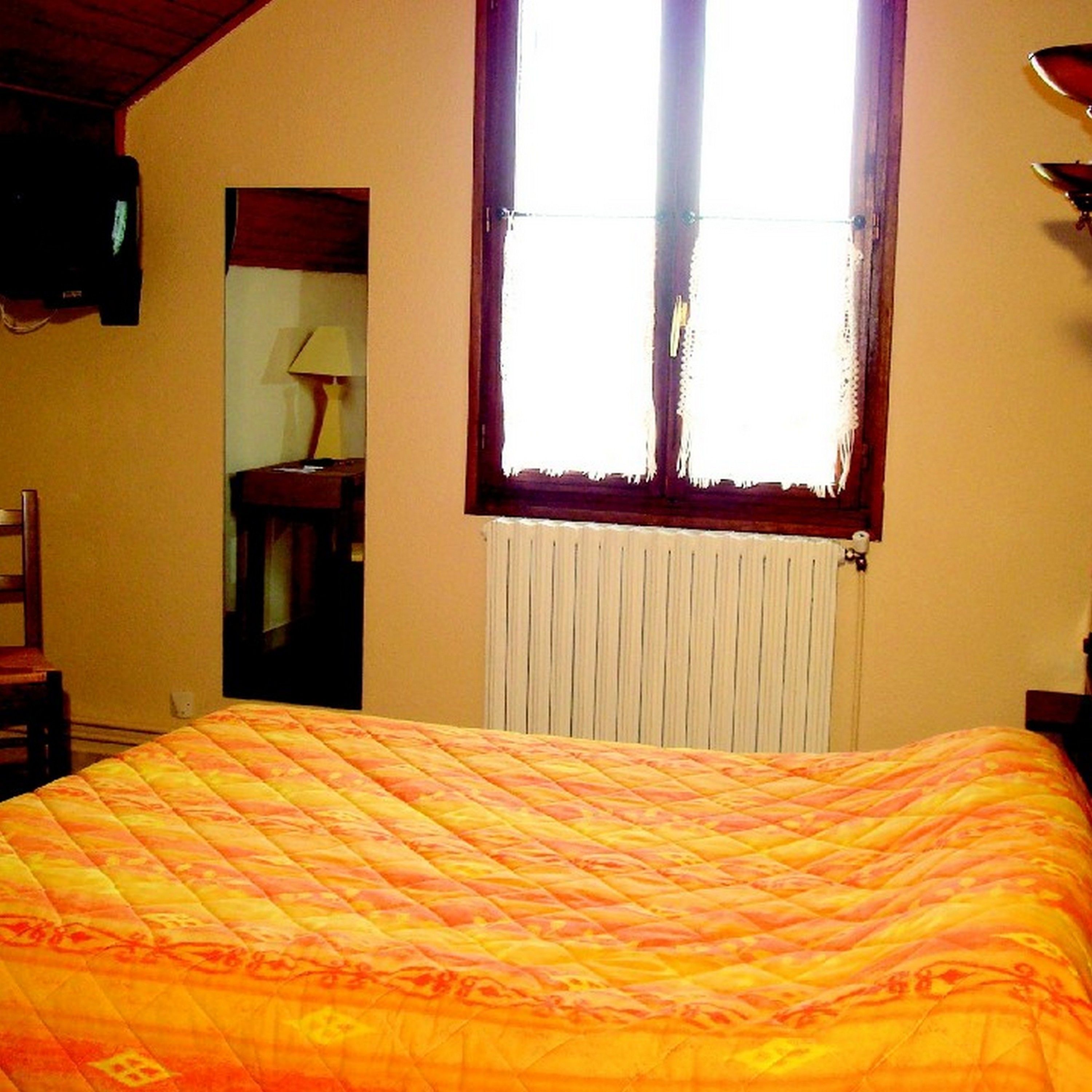 A bedroom with a bed, a window with curtains, a radiator, and a television on the wall.