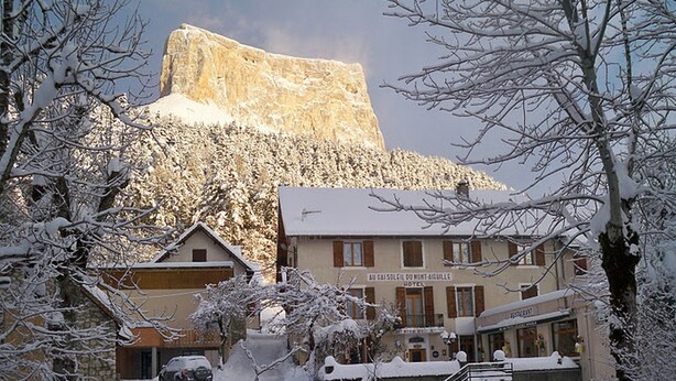 A hotel with a mountain backdrop, snow-covered trees, and a wooden fence in the foreground. - Au Gai Soleil du Mont Aiguille (Chichilianne)
