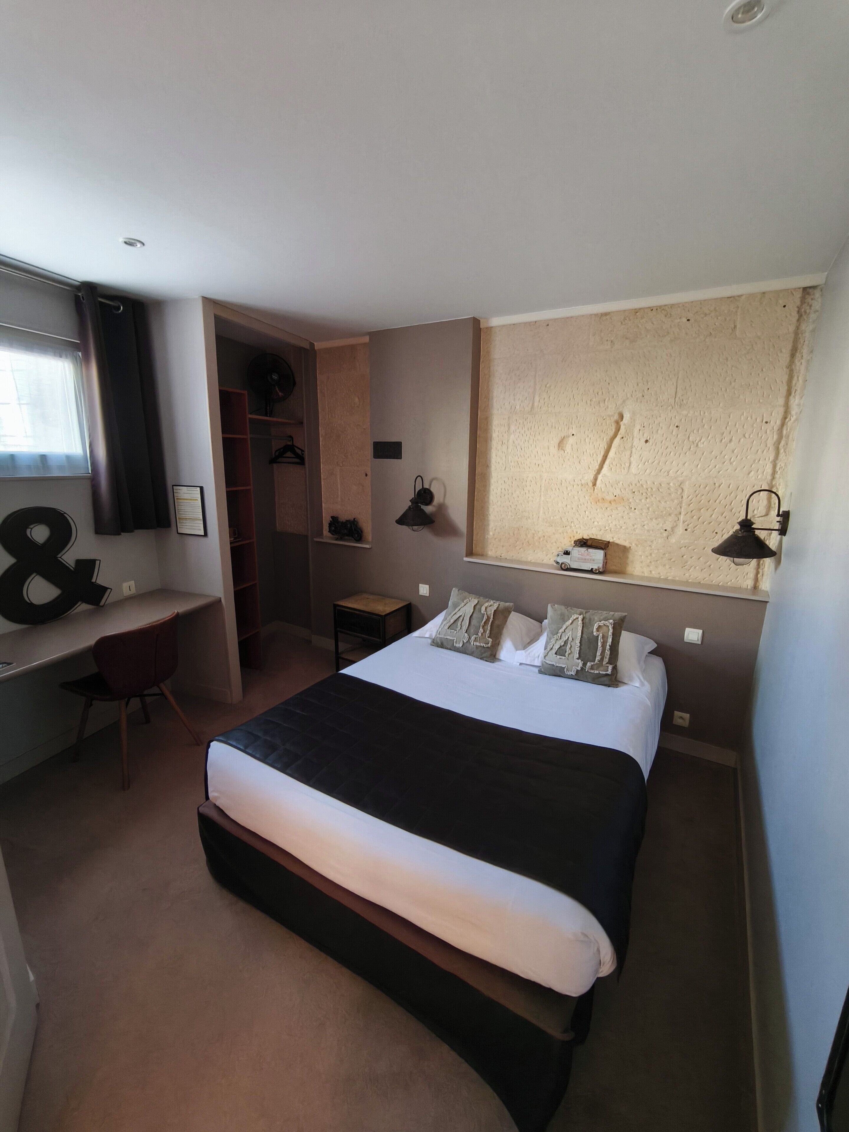 Ein Schlafzimmer mit Bett, Schreibtisch, Stuhl, Kleiderschrank und einem großen Fenster.