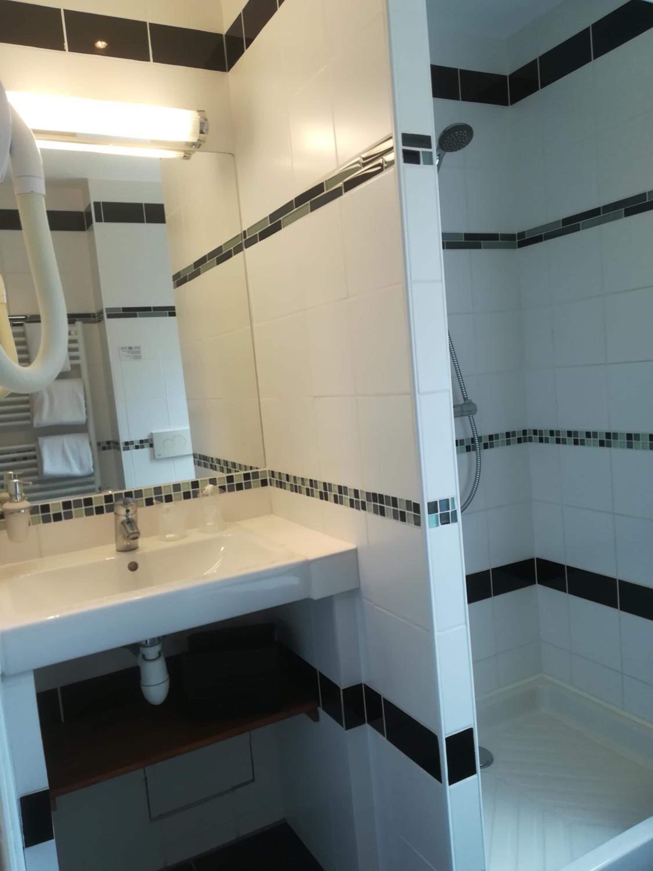 A bathroom with a white sink, a mirror, a towel rack, and a shower area with black and white tiles.