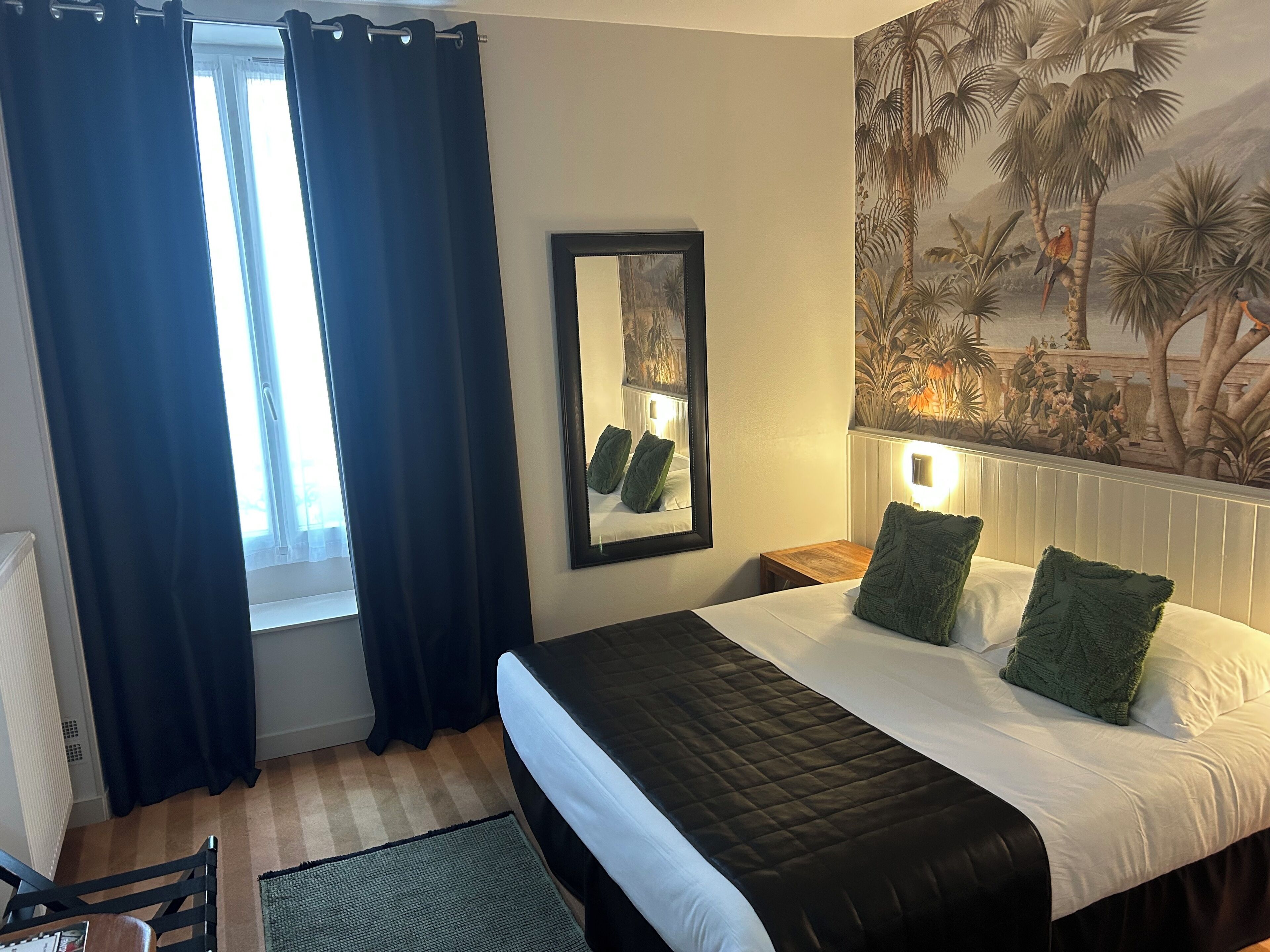 A hotel room with a bed, a nightstand, a mirror, and a window with curtains.