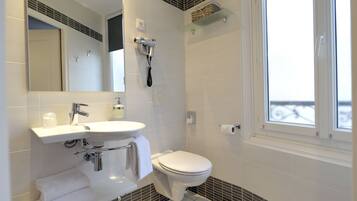 Un bagno moderno con lavandino bianco, specchio e water. Presente un portasciugamani con asciugamani piegati, un asciugacapelli montato a parete e una finestra con vista esterna.