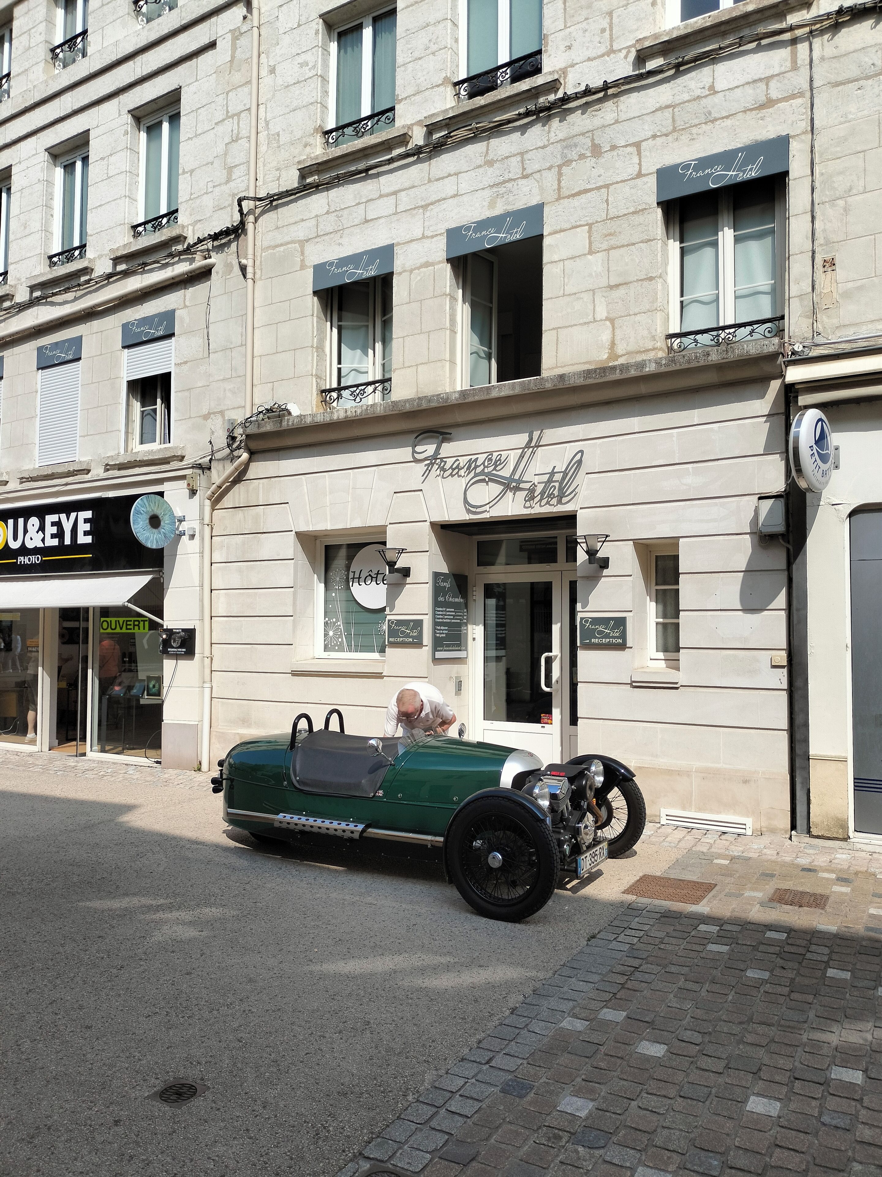 Un coche verde antiguo estacionado frente a un edificio con un letrero que dice 'France Hotel'.