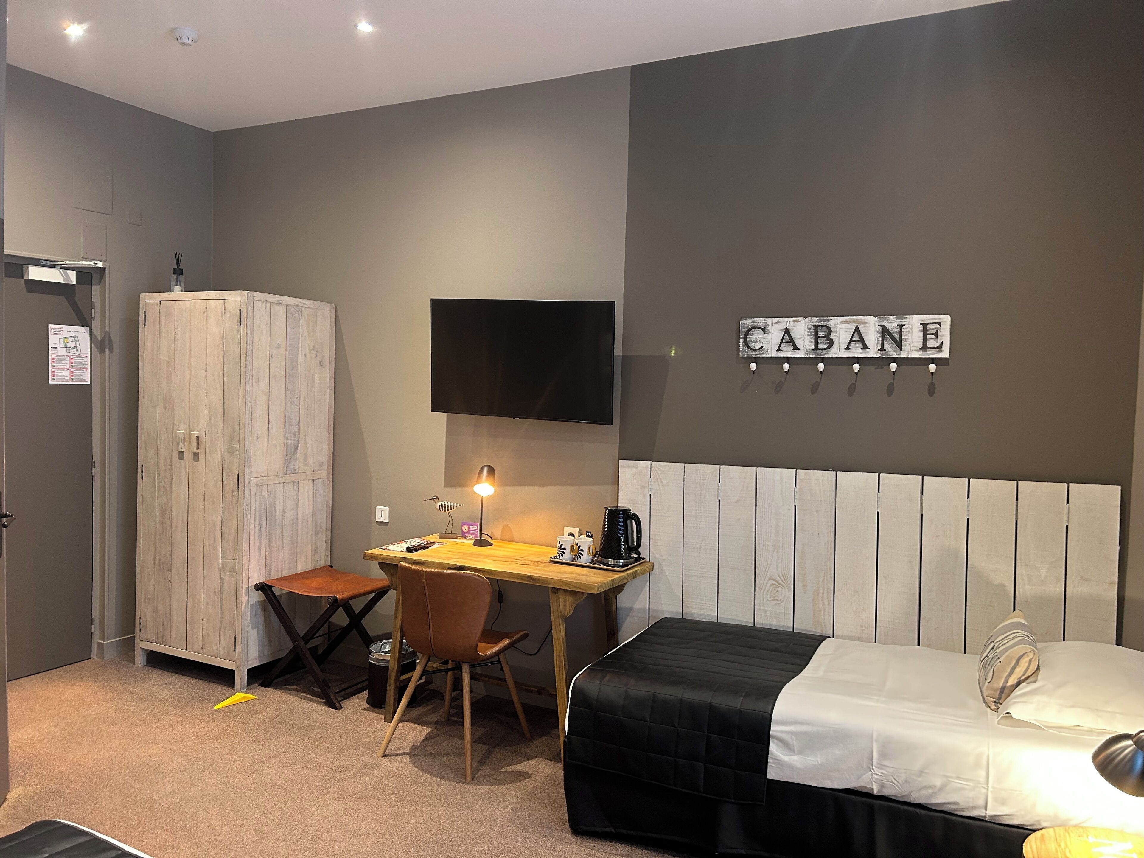 A small, modern room with a bed, a desk, and a wardrobe.