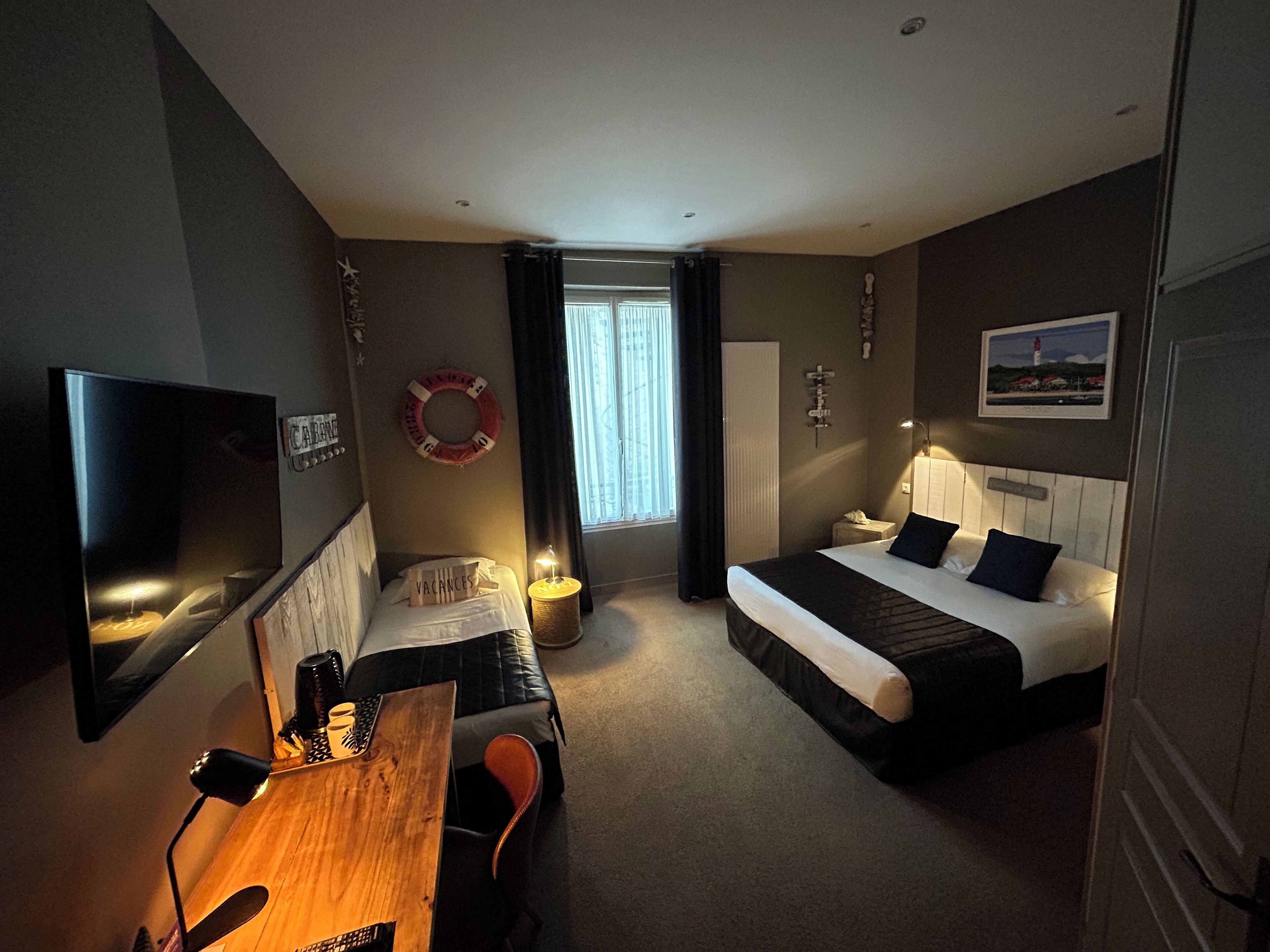 A hotel room with a bed, a desk, a chair, a TV, and a window with curtains.