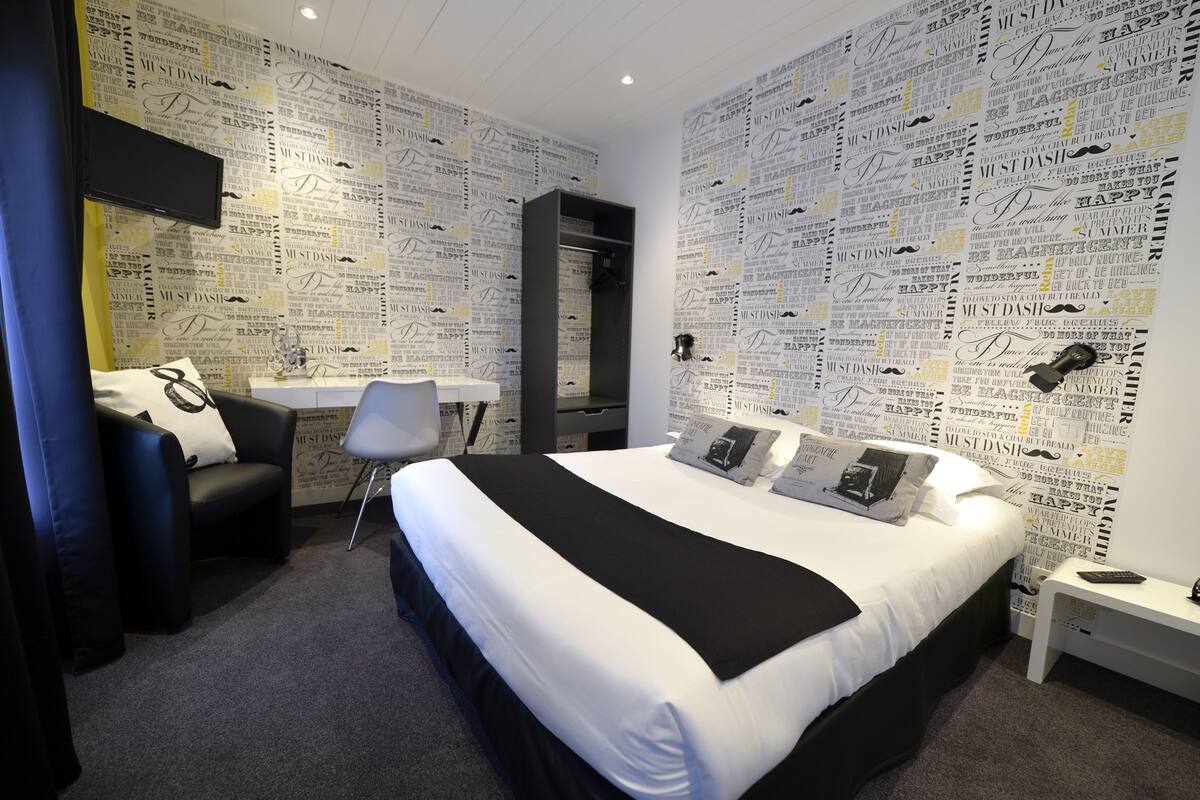 Habitación de hotel con una cama grande, un escritorio, una silla y una televisión en la pared.