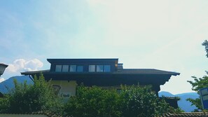 A modern building with a flat roof and large windows, surrounded by greenery and mountains in the background. - Pension Hilpold (Lana)