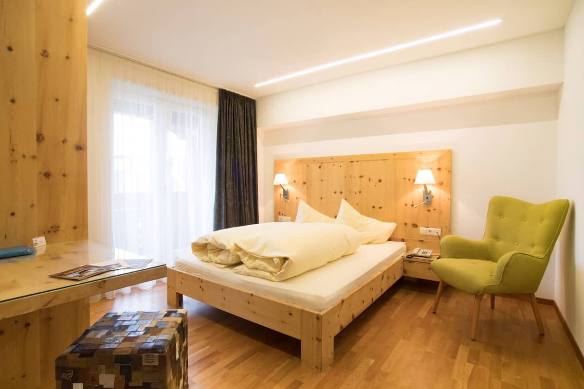 A wooden bed with a headboard, two bedside lamps, a green armchair, and a wooden nightstand with a lamp.