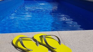 A pair of yellow flip-flops on a concrete surface near a swimming pool with clear blue water. - Pension Hilpold (Lana)