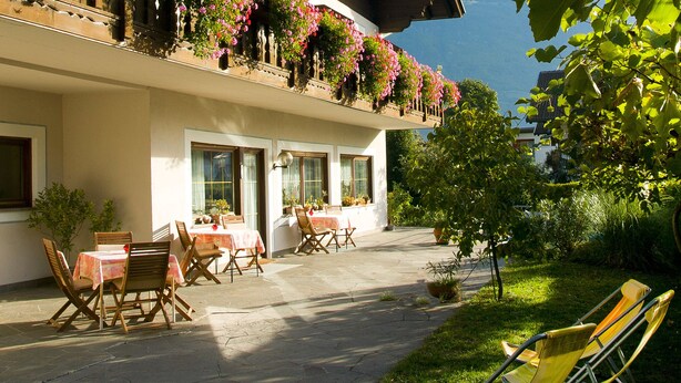 A hotel with outdoor seating, a balcony with flowers, and a view of the mountains. - Pension Hilpold (Lana)
