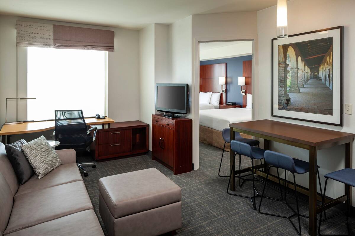 Habitación de hotel con sofá, escritorio y computadora, televisor, cama y zona de comedor con sillas.