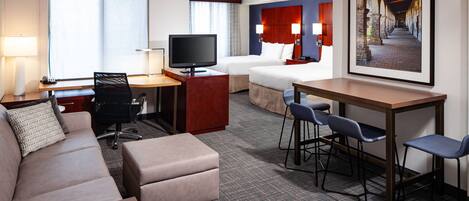 A hotel room with a sofa, a desk, a TV, a bed, and a dining area with chairs.