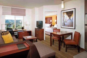 Habitación de hotel con sofá, escritorio con computadora, televisor, mesa de comedor con sillas y cama.