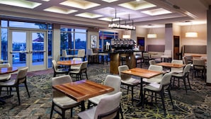 A hotel lobby with multiple seating areas, a bar, and large windows offering views of the outdoors.