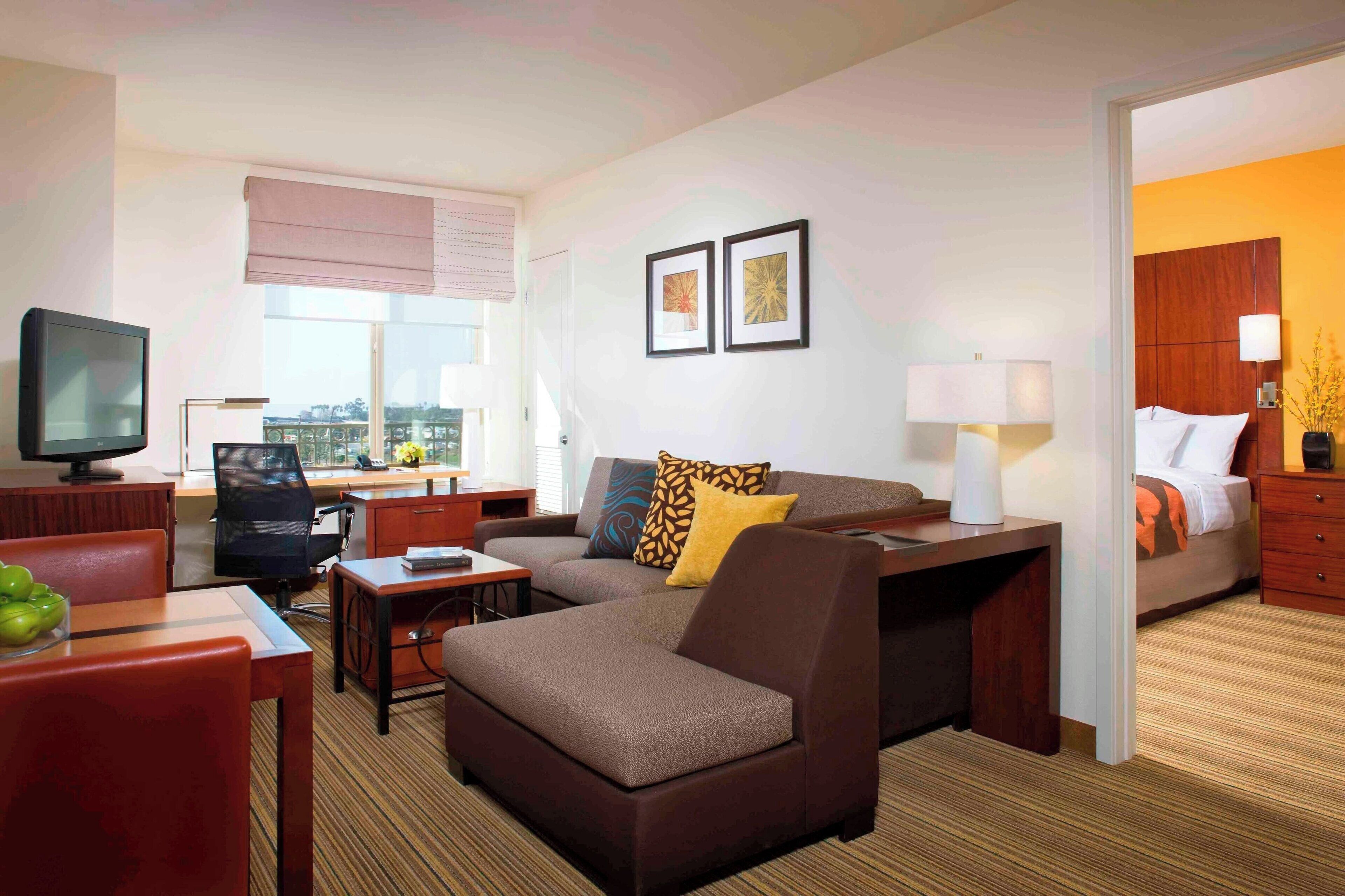 A hotel room with a sofa, armchair, desk, television, and a bed.
