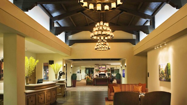 A spacious lobby with a high ceiling, a central chandelier, a fireplace, and a seating area with sofas and chairs.