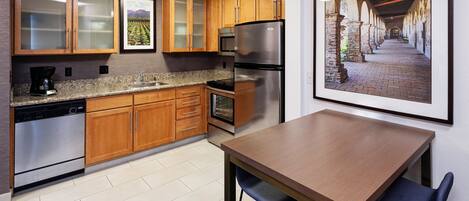 A modern kitchen with wooden cabinets, stainless steel appliances, a granite countertop, and a dining area with a table and chairs.
