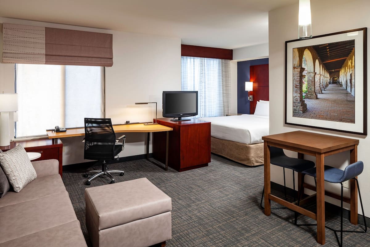 Habitación de hotel con cama, escritorio con computadora, televisor, sofá y pequeña mesa con sillas.