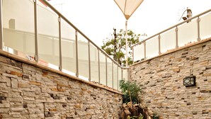 Un patio con paredes de piedra, muebles de mimbre y una mesa de vidrio.