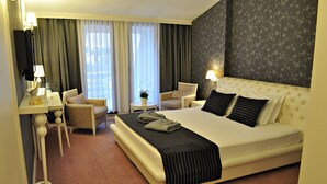 Habitación de hotel con una cama grande, dos sillas, una mesita pequeña y un escritorio con lámpara.