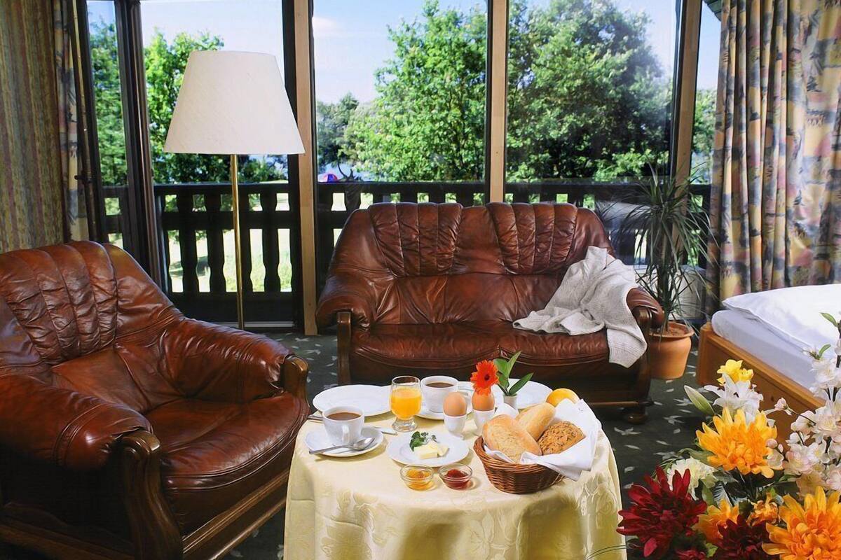 Un espacio al aire libre acogedor con dos sofás de cuero, una mesa de comedor con alimentos para el desayuno y vistas a zonas verdes a través de amplias ventanas.