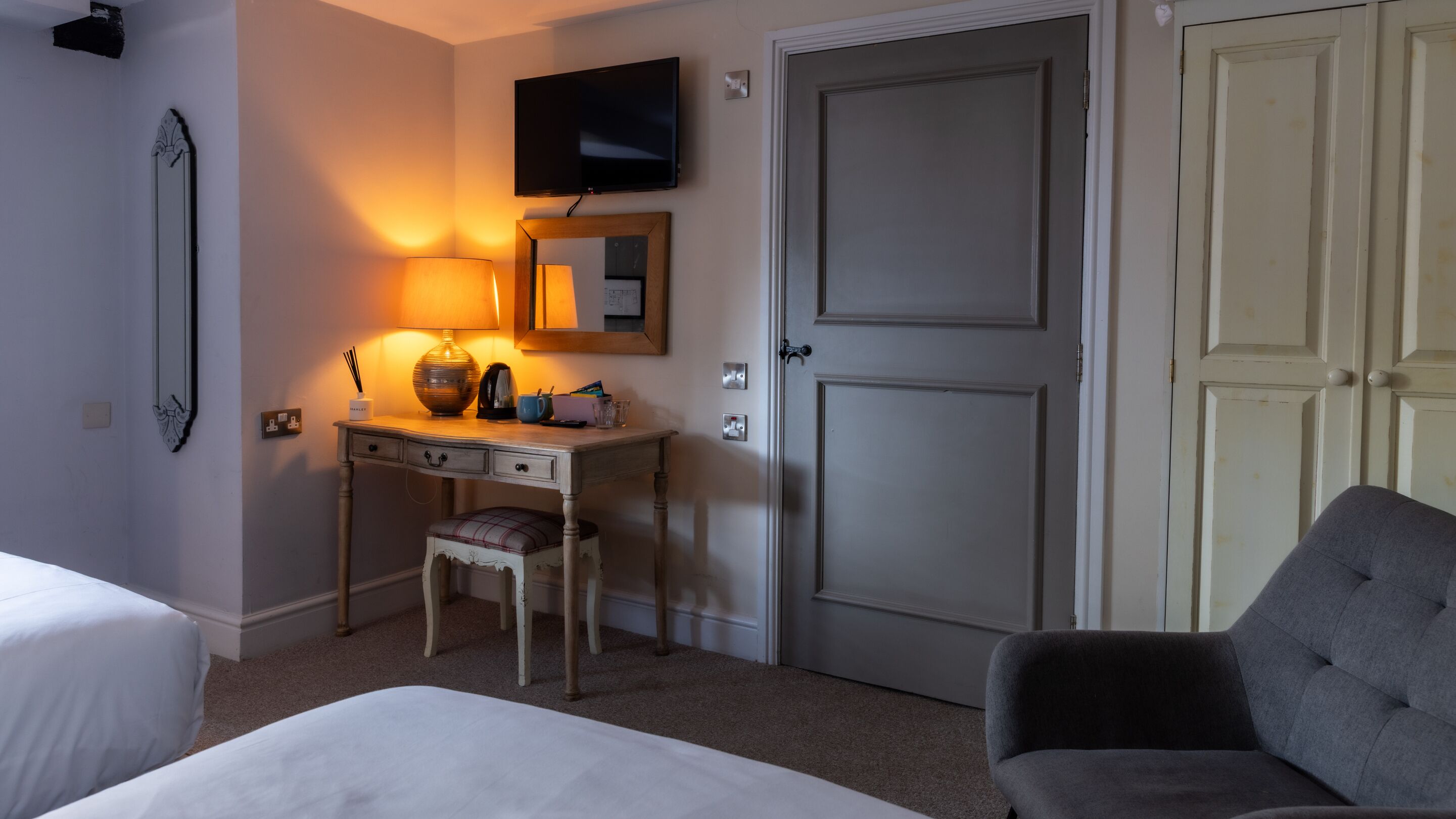 A hotel room with a bed, a desk with a lamp, a chair, a television, and a wardrobe.